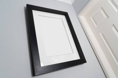 Duvara boş bir çerçeve, nötr renk şemasına sahip beyaz bir koridora yerleştirilmiş kalın siyah çerçevenin maketi.