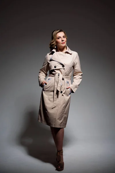 Woman in raincoat on gray background in studio.