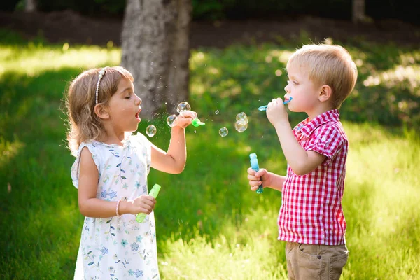 Five years old caucasian child girl and boy blowing soap bubbles