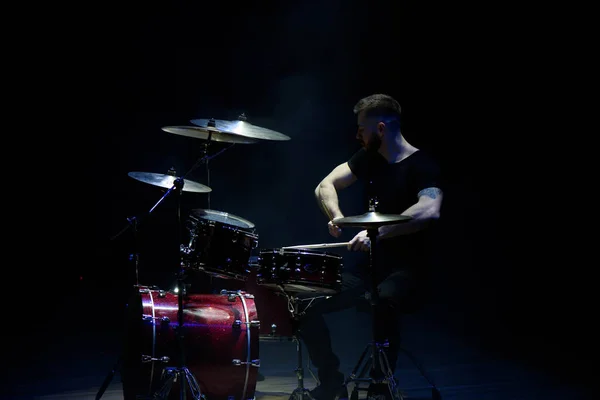 music, people, musical instruments and entertainment concept - male musician with drumsticks playing drums on the stage