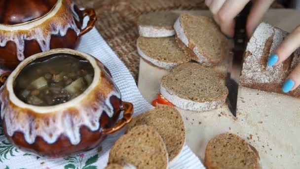 Una donna tagliata a pane. Nelle vicinanze c'è un cibo magro in una pentola . — Video Stock