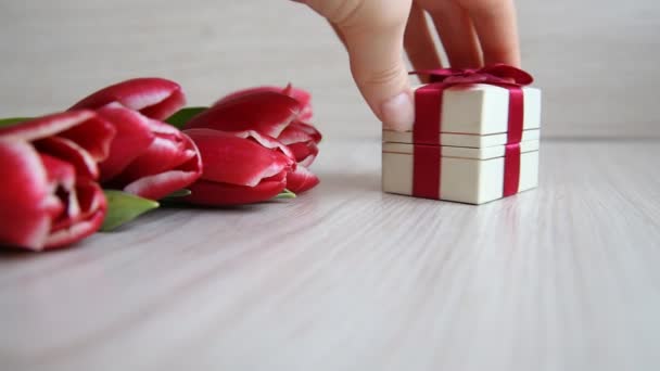 Hand shifts gift box with a red bow next to the tulips — Stock Video