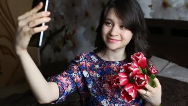 Vacker brunett flicka gör selfie med röda blommor tulpaner på svart smatfon. — Stockvideo