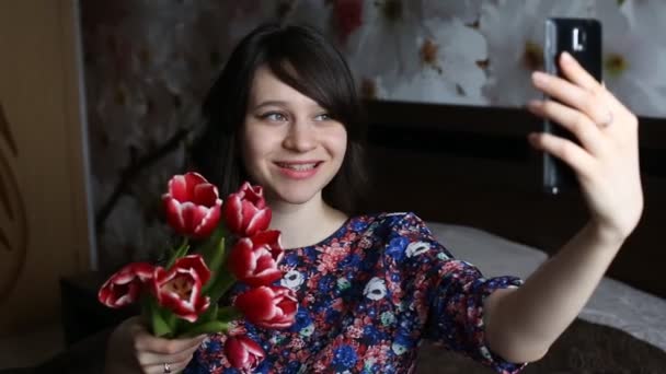 Beautiful brunette girl doing selfie with red flowers tulips on black smatfon. — Stock Video