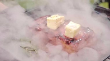 Tavada tereyağlı, dumanlı domuz bifteği, kömürleşmiş etin etrafında yükselen yoğun aromatik sis.