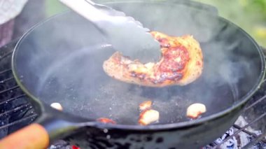 Kömürleşmiş kabuk için maşayla çevrilmiş tavuk tüttürme tavuğu, et yanında cızırdayan sarımsak karanfilleri, yoğun kavrulmuş