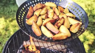 Ateşin üzerinde ızgara yapan yanmış patates parçaları, kızgın kömürlerin üzerinde tutulan ızgara tavası, dumanlı altın kabuk, yeşil