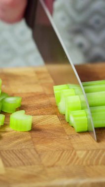 Güvertede doğranmış yeşil kereviz şeritleri, arka planda profesyonel mutfak titreşimleri, aşçı bıçağı çorba hazırlamak için düzgün küpler, parlak doku ve sabit ritim video fps