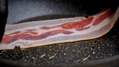 Çiğ pastırma hazırlığı. Tava yüzeyine pişirilmemiş pastırma. Pişmemiş pastırma dilimi, kahvaltıda pişirmek için yağlı, yapışmaz tavaya dikkatlice yerleştirilmiş.