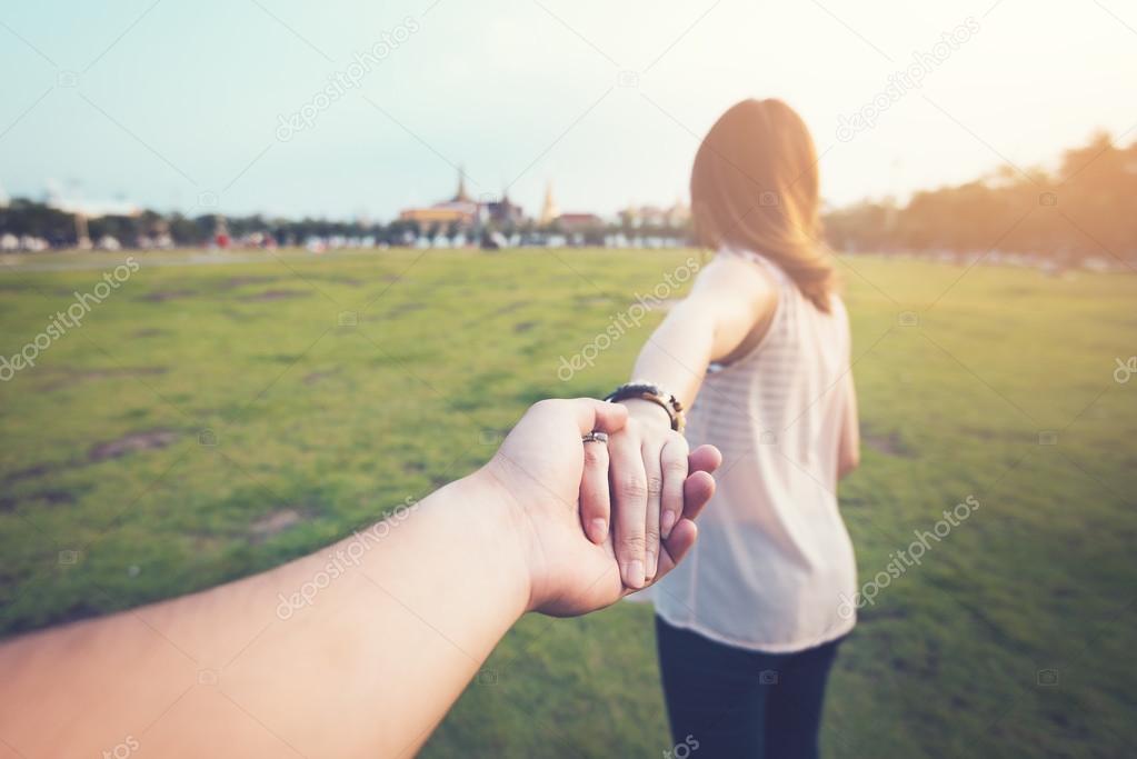 Young woman holding man hand on a greenfield. Focus on hands. couple in travel concept.