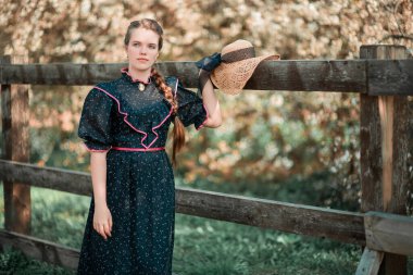 Parkta ağaçlarla birlikte çitlerin yanında poz veren genç bir kadın.