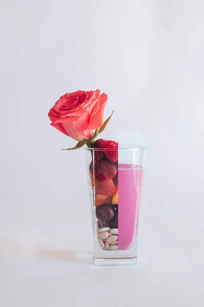 beautiful red rose in glass vase with fruits and berries, halved glass with smoothie on white background