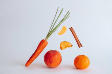 Havuç, mandalina, şeftali ve tarçın beyaz arka planda.