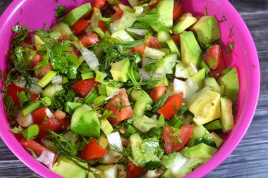 Bir kase yeşil salata, taze domates, salatalık, yeşil soğan, avokado, dereotu, maydanoz, marul ve pırasa, taze sebzelerden oluşan sağlıklı yeşil salata.