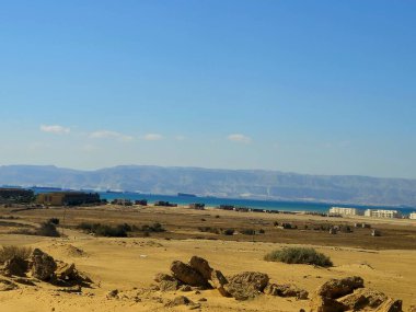 Ras Sedr, Güney Sina, Mısır, 17 Ocak 2026: Kızıl Deniz 'in sularına doğru çöl manzarası, kıyıda bir dağ, binalar ve yapılar ve su üzerinde gemiler.