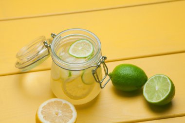 Buz, limon ve kireç üzerinde sarı bir ahşap ba bir kavanoza ile limonata