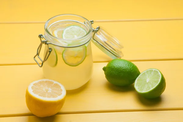 Limonade mit Eis, Zitrone und Limette im Glas auf gelbem Holzboden — Stockfoto