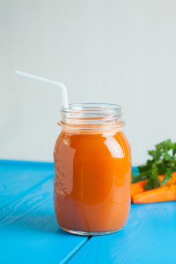 Sağlıklı havuç elma güler yüzlü bir kavanoza mavi ahşap zemin üzerine