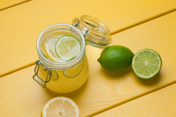 Limonada com gelo, limão e limão em um jarro em uma ba de madeira amarela — Fotografia de Stock