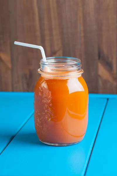 Sağlıklı havuç elma güler yüzlü bir kavanoza mavi ahşap zemin üzerine