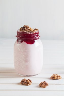 Reçel ve bir beyaz tahta üzerinde bir kavanoza ceviz ile ev yapımı yoğurt 