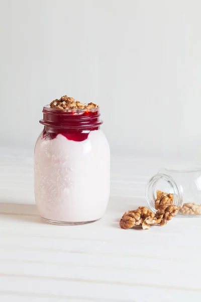 Reçel ve bir beyaz tahta üzerinde bir kavanoza ceviz ile ev yapımı yoğurt 