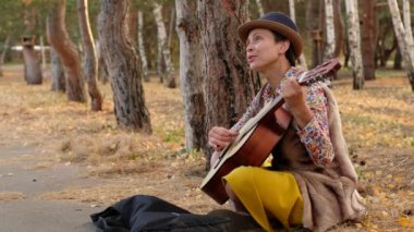 Parkta akustik gitar çalan şapkalı güzel bir kadın. Sokak müzisyeni bir şarkı söyler ve para ister..
