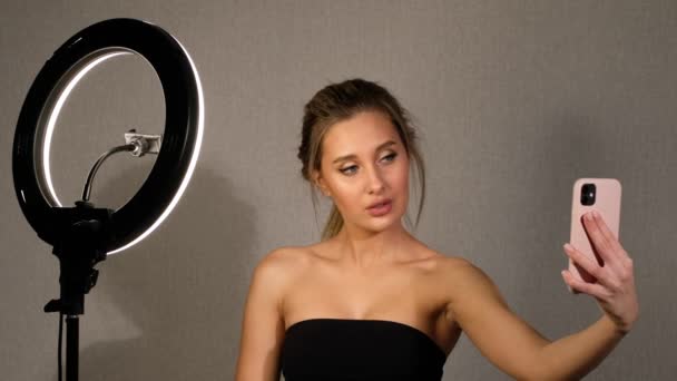 Vacker kvinna tar en selfie på sin telefon på ringlampa i studio. Modern flicka tar bilder makeup för sociala nätverk. — Stockvideo