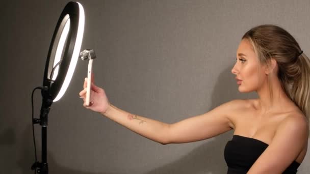 Όμορφη γυναίκα βγάζει μια selfie στο τηλέφωνό της στο ring lamp στο στούντιο. Σύγχρονη κοπέλα λήψη φωτογραφιών μακιγιάζ για τα κοινωνικά δίκτυα. — Αρχείο Βίντεο