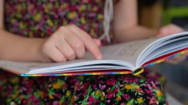 Renkli elbiseli küçük kız kitap okuyor. Çocuk okumayı öğreniyor..