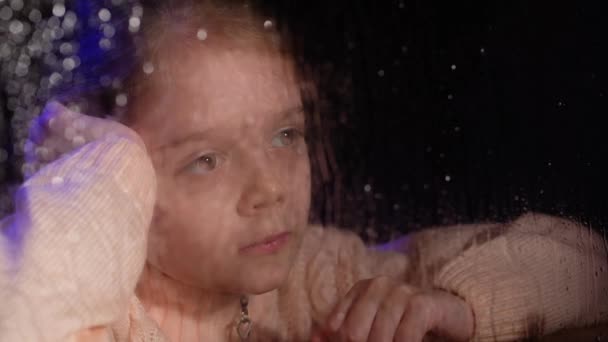Barnet sitter hemma och tittar på regn. Dåligt väder utanför fönstret. — Stockvideo