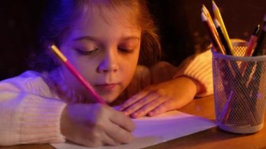 Çocuk masada otururken kurşun kalemle bir kalp çizer. Küçük kız akşamları pencerenin yanında sevgililer günü kartı çiziyor..