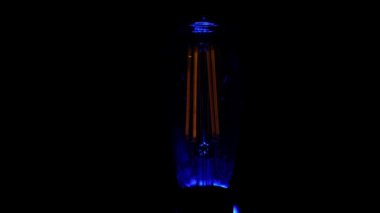 Retro vintage Edison ampulü yanıp sönüyor ve siyah arkaplana karşı açılıyor.