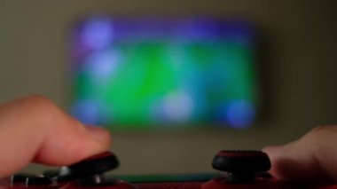 Oyuncu elleri oyun konsolunda joystick kullanarak futbol simülatörü oyunu oynuyor.