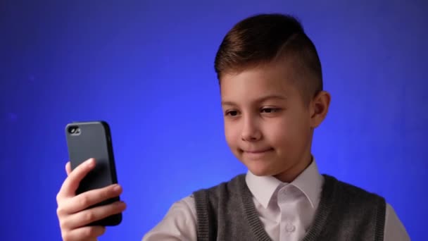 Knappe schooljongen neemt een selfie op zijn telefoon. Modern kind wordt gefotografeerd op zijn smartphone. — Stockvideo