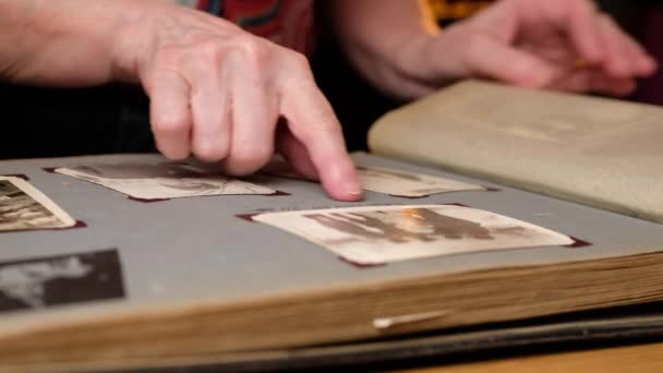 Idős nő átnéz egy családi albumot régi fotókkal az asztalnál otthon. — Stock videók