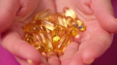 Kadın balık yağı kapsüllerini elinde tutuyor. Sarı omega 3 hapları..