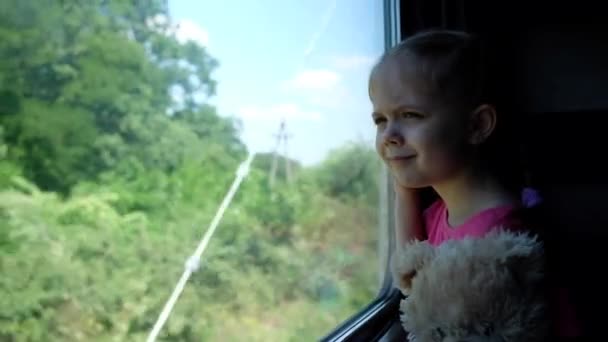 Dítě bude pršet u okna. Holčička cestuje s plyšovým medvědem se dívá na železnici. — Stock video