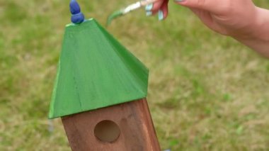 Kadın ağaç parkındaki kuşlar için bir kuş evinin çatısını boyuyor..