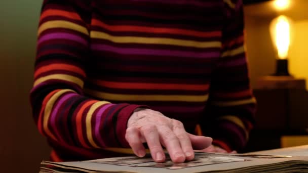 Femme âgée regarde à travers un album de famille avec de vieilles photos à la table à la maison. — Video