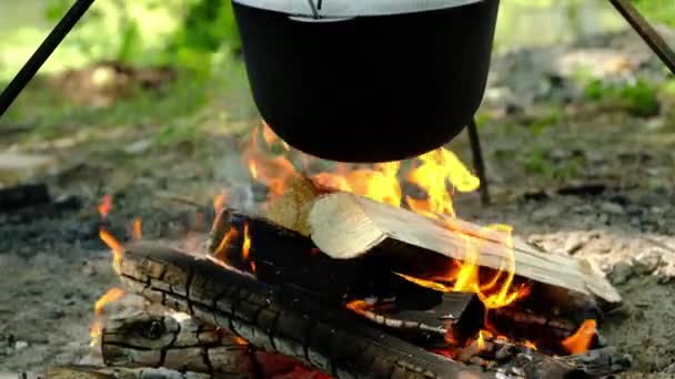 Les gens préparent le déjeuner dans un pot de randonnée sur le feu de camp au camp. Bowler sur le feu de joie. — Video