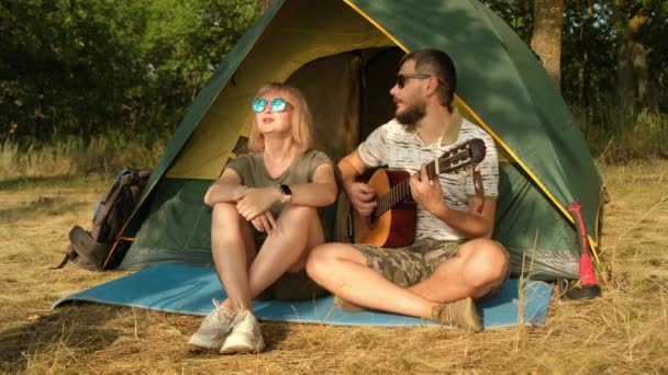 Чоловік і жінка співають пісню з гітарою, сидячи в наметі. . — стокове відео