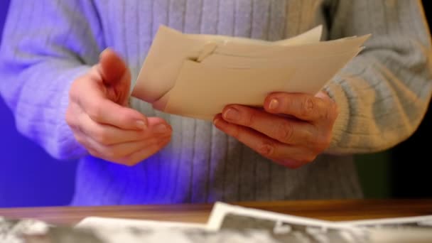 Mujer anciana mira fotos viejas sentadas en una mesa en casa. — Vídeos de Stock