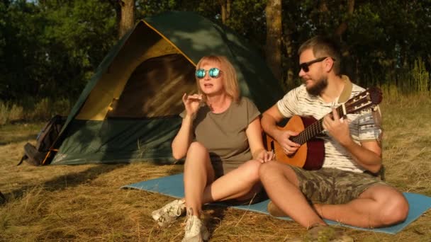 Homme et femme chantent la chanson avec guitare assis à la tente.Touristes est en voyage de camping. — Video