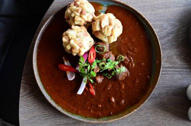 Geleneksel Çek geyik kebabı, kırsal bir ahşap masada bir restoranda servis edilir. Yemek güzel bir şekilde ekmekli börek, karamelli soğan ve dekorasyon için kırmızı biber ile sunuluyor.
