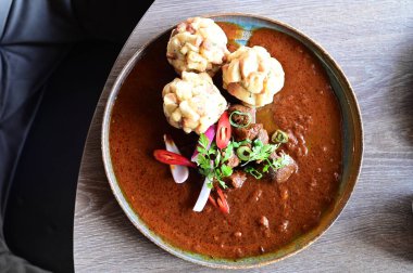 Geleneksel Çek geyik kebabı, kırsal bir ahşap masada bir restoranda servis edilir. Yemek güzel bir şekilde ekmekli börek, karamelli soğan ve dekorasyon için kırmızı biber ile sunuluyor.