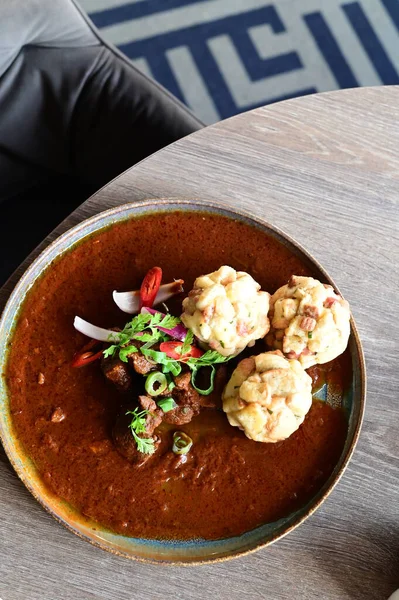 Geleneksel Çek geyik kebabı, kırsal bir ahşap masada bir restoranda servis edilir. Yemek güzel bir şekilde ekmekli börek, karamelli soğan ve dekorasyon için kırmızı biber ile sunuluyor.