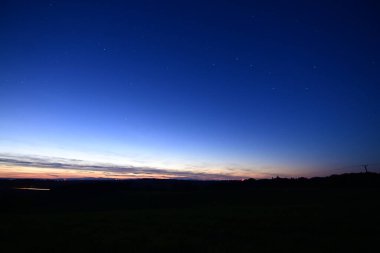 Büyük Ayı takımyıldızı, kuyruklu yıldız Lemmon ve yıldız bağlantı uydularıyla dolu renkli bir ufukta gün batımı..