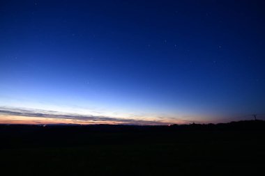 Büyük Ayı takımyıldızı, kuyruklu yıldız Lemmon ve yıldız bağlantı uydularıyla dolu renkli bir ufukta gün batımı..