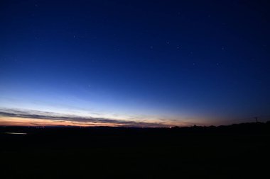 Büyük Ayı takımyıldızı, kuyruklu yıldız Lemmon ve yıldız bağlantı uydularıyla dolu renkli bir ufukta gün batımı..